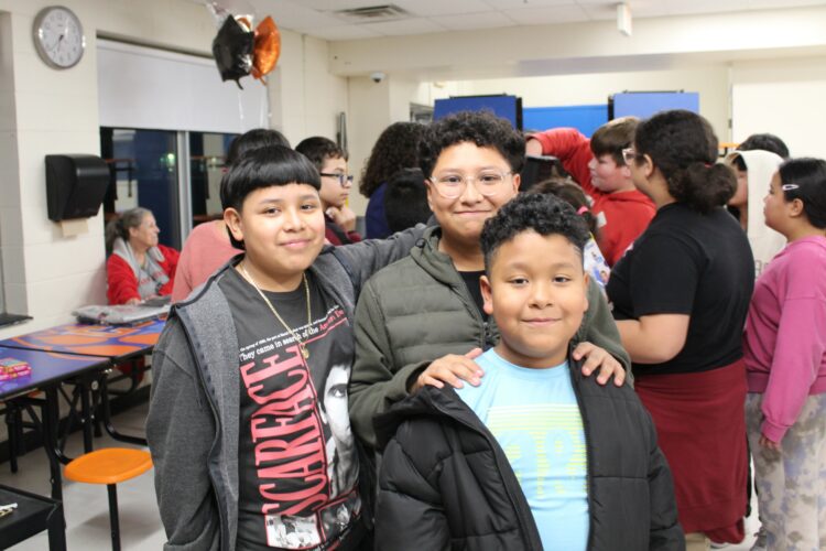 Three students pose in front of the raffle at math night.