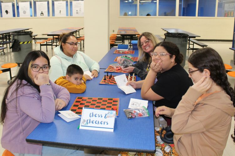 Three Cowherd students pose with their family and a teacher while playing chess and checkers.